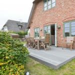 Terrasse mit Tisch und Stühlen an Backsteinhaus mit grünen Fenstern.
