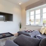 Wohnzimmer mit Sofa, Fernseher und Fenster mit Blick auf Grünflächen.