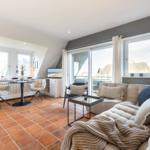 Wohnbereich mit Sofa, Tisch und Fenstern. Terrasse und Blick auf Dächer.