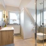 Badezimmer mit Dusche, Waschbecken und Toilette unter Dachschräge