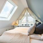 Schlafzimmer mit Dachschrägen, Dachfenster und Fenster mit Vorhängen.
