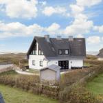 Modernes Haus mit dunklem Dach und weißer Fassade, umgeben von Grünflächen und Strand.