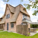 House with thatched roof, garden, and terrace with table and chairs.