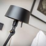 Black floor lamp next to bed with wall art and outlet.