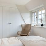 Bedroom with bed, chair, and window. White wall and wardrobe.