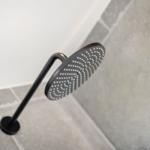 Showerhead with black metal stand on gray tiled floor.