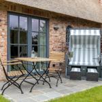 Terrace with table, chairs, and beach chair in front of brick house with thatched roof.