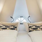 Two beds with pillows under a window in an attic room.