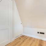Room with wooden floor, white door, and sloped wall