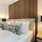 Bedroom with bed, wooden wall, and nightstand with lamp.