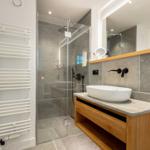 Modern shower with glass enclosure, sink with mirror and towel heater on wall.