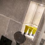 Shower cabin with shower head and three yellow care products in stone niche.