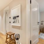 Hallway with wooden floor, stool, and artwork. View into living room with sofa and rug.