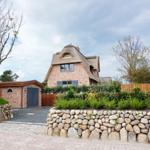 House with thatched roof, stone wall, and paved driveway