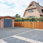 House with thatched roof, wooden fence, and gravel area