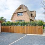 House with thatched roof, wooden fence, and gravel driveway.