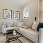 Living room with sofa, coffee table, and window. Wall art and floor lamp visible.