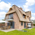 House with thatched roof and terrace with garden furniture.