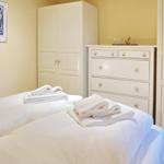 Two beds with white linens and towels. White wardrobe and dresser. Wall art by Matisse.