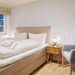 Bedroom with bed, nightstand, and chair. Wall with striped pattern.