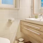 Bathroom with sink, mirror, and toilet. Wooden cabinet and toilet paper holder visible.
