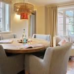 Round wooden table with chairs, seating area, and windows in dining space.