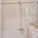 Bath with shower, white tiles, and glass wall. On the sink is a golden seashell figurine.