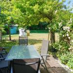 Garden with seating, flowers, and tree. Background with lawn and house.