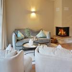 Living room with sofa, fireplace, and two armchairs. Window and wall lighting visible.