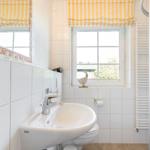 Bathroom with sink, toilet, and shower. Window with yellow-white roller blind.