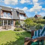 House with balcony, garden, and beach chairs under blue sky.