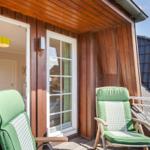 Terrace with two green chairs in front of wooden house with glass door.
