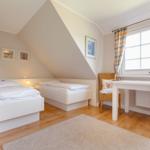 Room with two beds, desk and window with curtain.