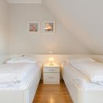 Two single beds with white bedding and nightstand under sloped ceiling