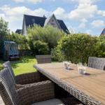 Deck with wooden table and chairs, lawn area and beach chair in background.