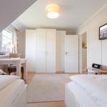 Room with two beds, desk, and wardrobe under sloped ceiling.