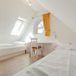 Room with sloped ceiling, two beds, desk, and windows.