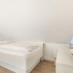 A bedroom with a white bed, wooden floor, and TV on a cabinet.