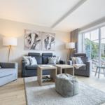 Living room with gray chairs, sofa, and cushions. Large window view to garden.