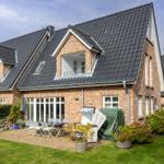 House with terrace, garden and wooden terrace. White windows and gray roof ridge.