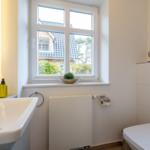 Bathroom with sink, toilet, and window with view of house and trees.