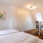 Bedroom with bed, wardrobe, and desk under sloped ceiling.