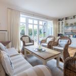 Living room with sofa, rattan chairs, and TV unit. Large windows with view outside.