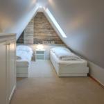 Two single beds in an attic room with wooden wall and skylight.