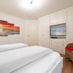 Bedroom with white bed, built-in TV, and wicker chair