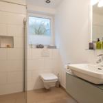 Bathroom with shower, sink and toilet. Window with plant.
