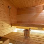 Sauna with wooden bench, bucket, and thermometer on the wall.