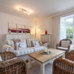 Living room with sofa, wicker chairs, and large window to the garden.