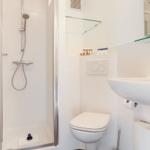 Dusche mit Handbrause, Toilette und Waschbecken mit Spiegel.