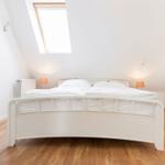 Schlafzimmer mit Dachfenster, weißem Bett und Holzboden.